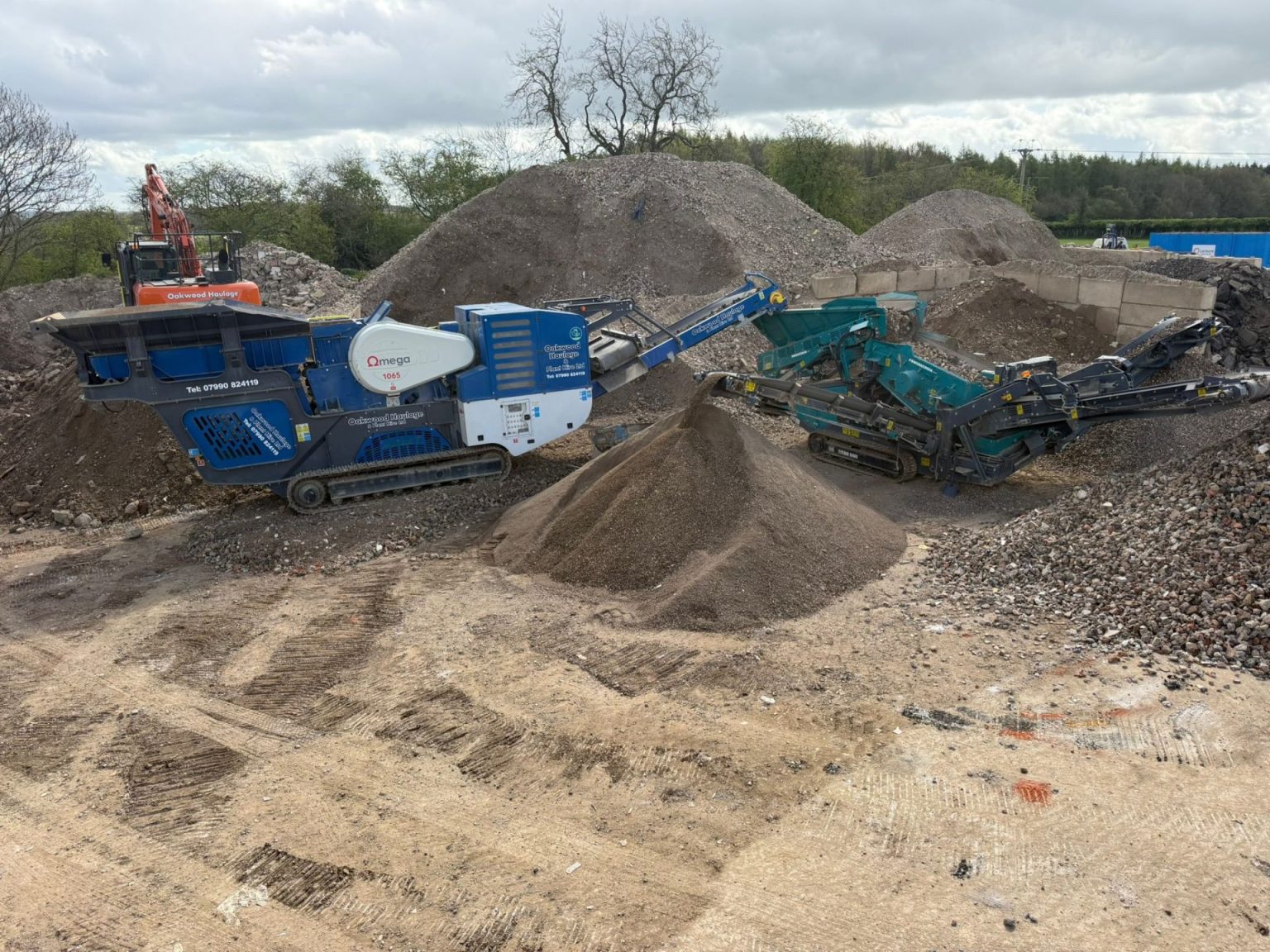 Blue mobile crusher and screener processing aggregates at an outdoor recycling yard